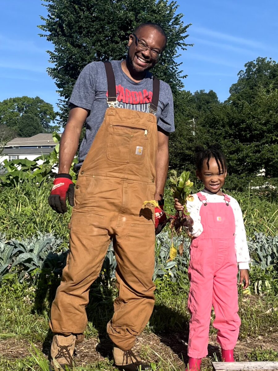 Frank Whitfield in work overalls at the farm with a young helper holding freshly harvested beets